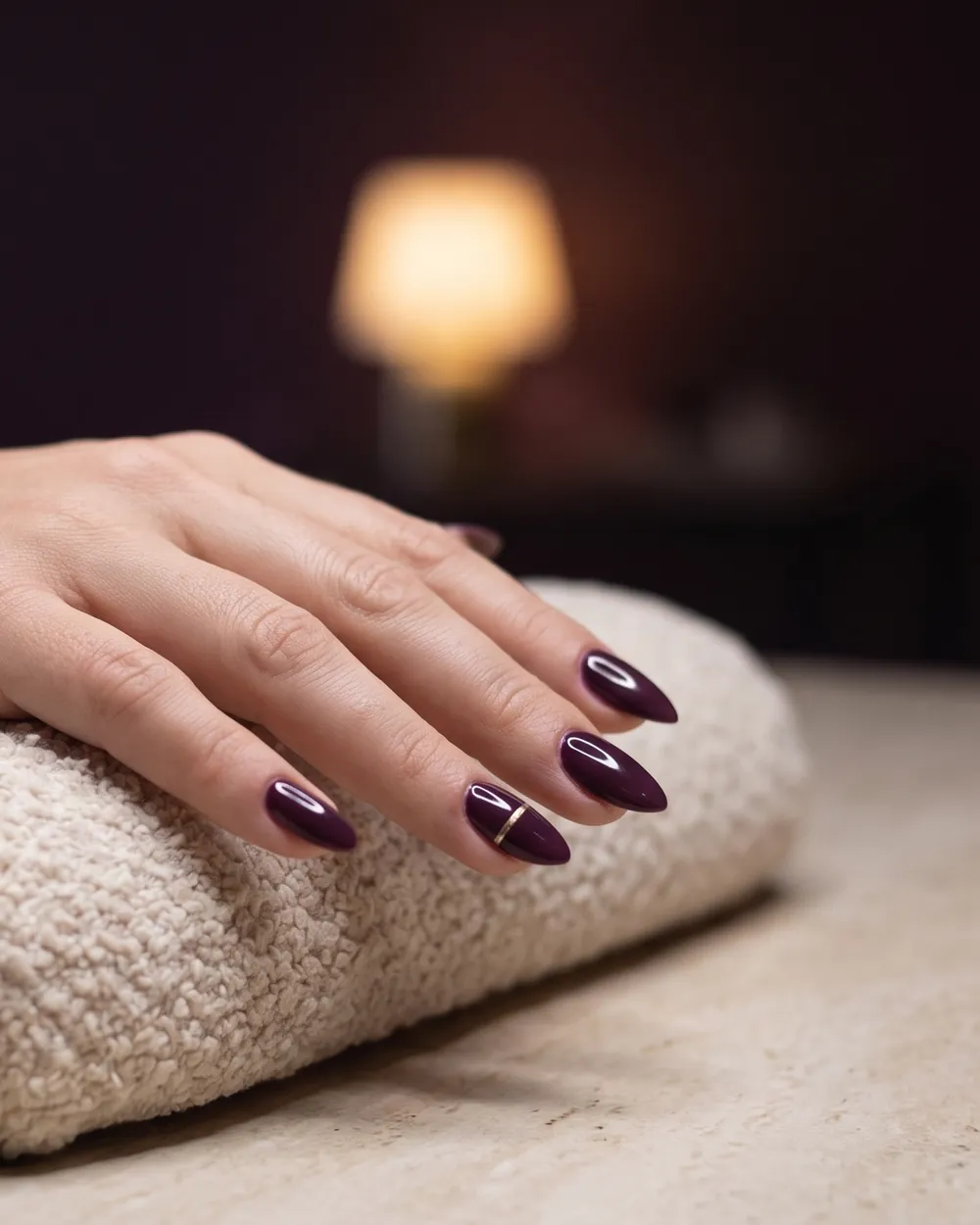 A hand with finished glossy plum nails resting on a cream cushion